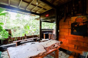 A rustic wooden room with a bench, a brick wall with a mural, and a view of lush greenery outside.