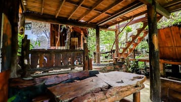 A rustic wooden structure with a bench and a table, surrounded by natural vegetation.