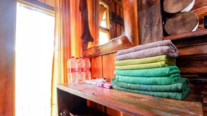 A wooden shelf with stacked towels and plastic bottles. - Rimbono Homestay (Kalirejo)