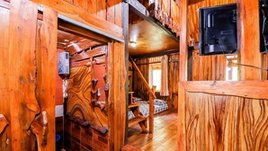 A wooden cabin interior with a bunk bed, a wooden staircase, and a television mounted on the wall. - Rimbono Homestay (Kalirejo)