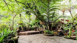 A garden with a stone pathway, wooden benches, and a statue. - Rimbono Homestay (Kalirejo)