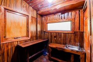 A rustic wooden cabin interior with a wooden bench, a sink, and a window. - Rimbono Homestay (Kalirejo)