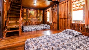 A rustic wooden cabin with a wooden staircase, two beds with patterned bedding, and a large window with curtains. - Rimbono Homestay (Kalirejo)