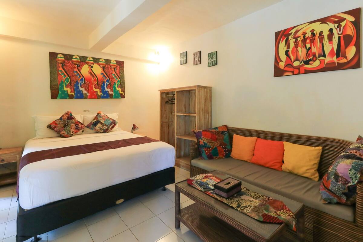A hotel room with a bed, a sofa, a coffee table, and artwork on the walls.