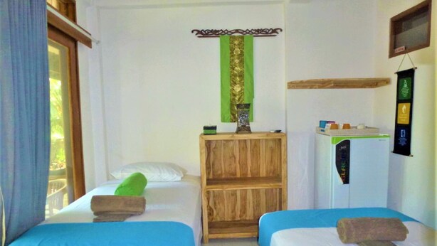 A hotel room with two beds, a wooden nightstand, a refrigerator, and a window with curtains.