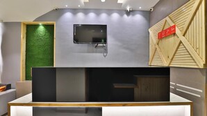 Uma área de recepção moderna com uma televisão de tela plana na parede, um balcão de madeira e uma parede verde com textura.
