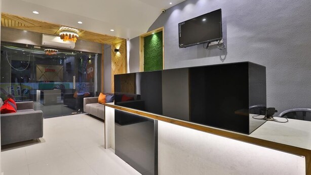 Uma área de recepção moderna com divisória de vidro, sofás cinza, design de teto em madeira e uma TV na parede.
