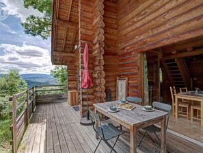 Une cabane en bois dotée d’une terrasse, d’une table à manger avec des chaises et offrant une vue sur le paysage.