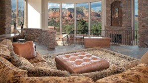 Amplia sala de estar con una chimenea de piedra grande, un muro decorativo de piedra y vistas a formaciones rocosas rojas.