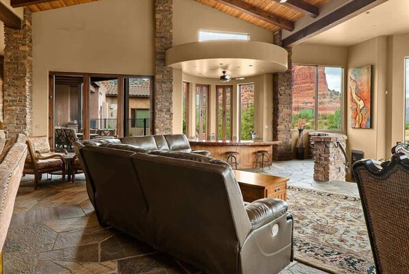 A spacious living area with a stone fireplace, leather seating, and a large window overlooking a mountainous landscape.