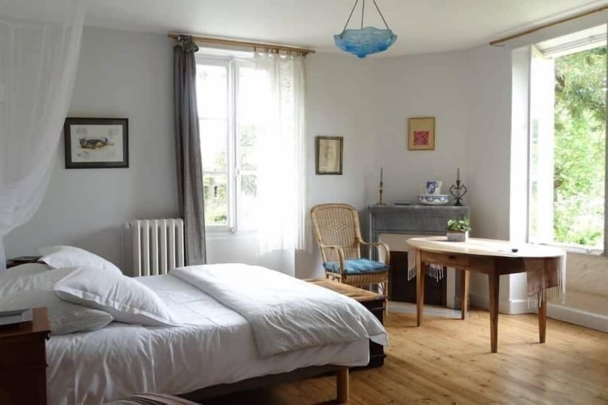 A bedroom with a bed, a chair, a table, and a window.