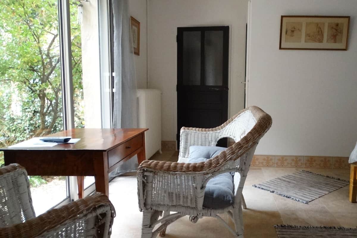 A room with a wooden desk, wicker chair, a bed, and a door.