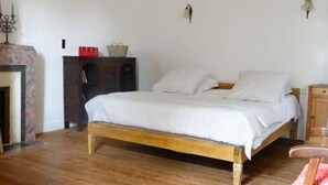A bedroom with a wooden bed, white bedding, a nightstand, a wooden wardrobe, and a small table with a red bowl and a woven basket. - Moulin de la Papeterie Chambres d'hôtes (La Creche)
