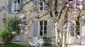 A building with white shutters, a garden with pink flowers, and outdoor furniture. - Moulin de la Papeterie Chambres d'hôtes (La Creche)
