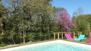 A swimming pool with a wooden deck and colorful lounge chairs. - Moulin de la Papeterie Chambres d'hôtes (La Creche)