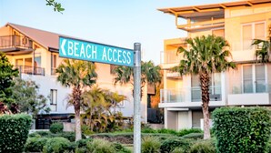 A street sign reading "Beach Access" with modern buildings and palm trees in the background.