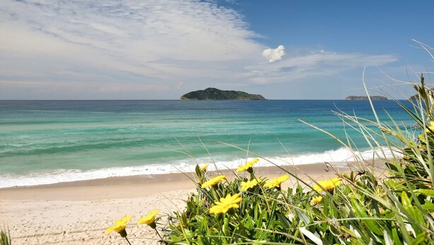 A beach with clear turquoise waters, a sandy shore, and a small island in the distance.