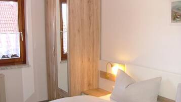 Quarto com cama, mesa de cabeceira, abajur, guarda-roupa e janela.