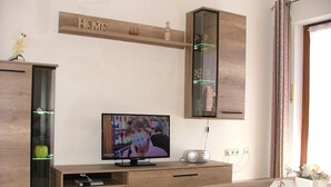 A living room with a television, wooden entertainment unit, and a bookshelf. - Haus Gertrud (Wittmund)