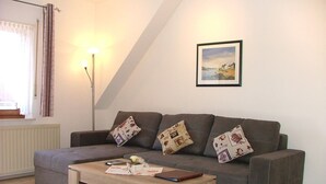A cozy living room with a grey sofa, three patterned cushions, a wooden coffee table, and a framed picture on the wall. - Haus Gertrud (Wittmund)