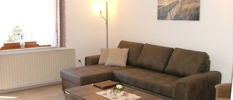 A living room with a brown sofa, a wooden coffee table with a remote control, a lamp, and a painting on the wall.