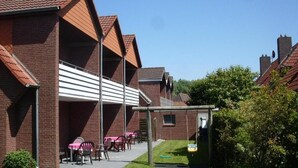 A brick building with a covered patio area, outdoor seating, and a swing set. - Haus Gertrud (Wittmund)