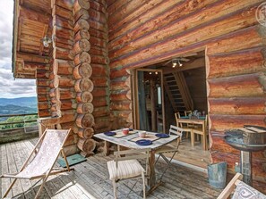 Una cabaña de troncos con un balcón, una mesa de comedor con sillas y una escalera que sube a un nivel superior.