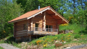 Une cabane en rondins dotée d’un balcon, entourée de verdure et de fleurs.