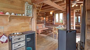 L’intérieur d’une cabane en rondins, avec une cheminée, des meubles en bois et une étagère remplie d’ustensiles de cuisine.