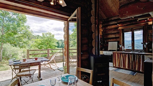 Une cabane en bois comprenant un coin repas, une cuisine et une grande fenêtre donnant sur une forêt.