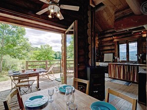 Una cabaña de madera con comedor, cocina y un ventanal grande con vistas a un bosque.