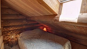 L’intérieur d’un chalet en bois, avec un plafond en pente, une lucarne, un lit et une lampe de style lanterne.