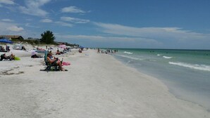 A beach with people sunbathing and swimming, umbrellas, and beach chairs.