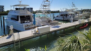A marina with several boats docked, a wooden pier, and a clear blue sky.