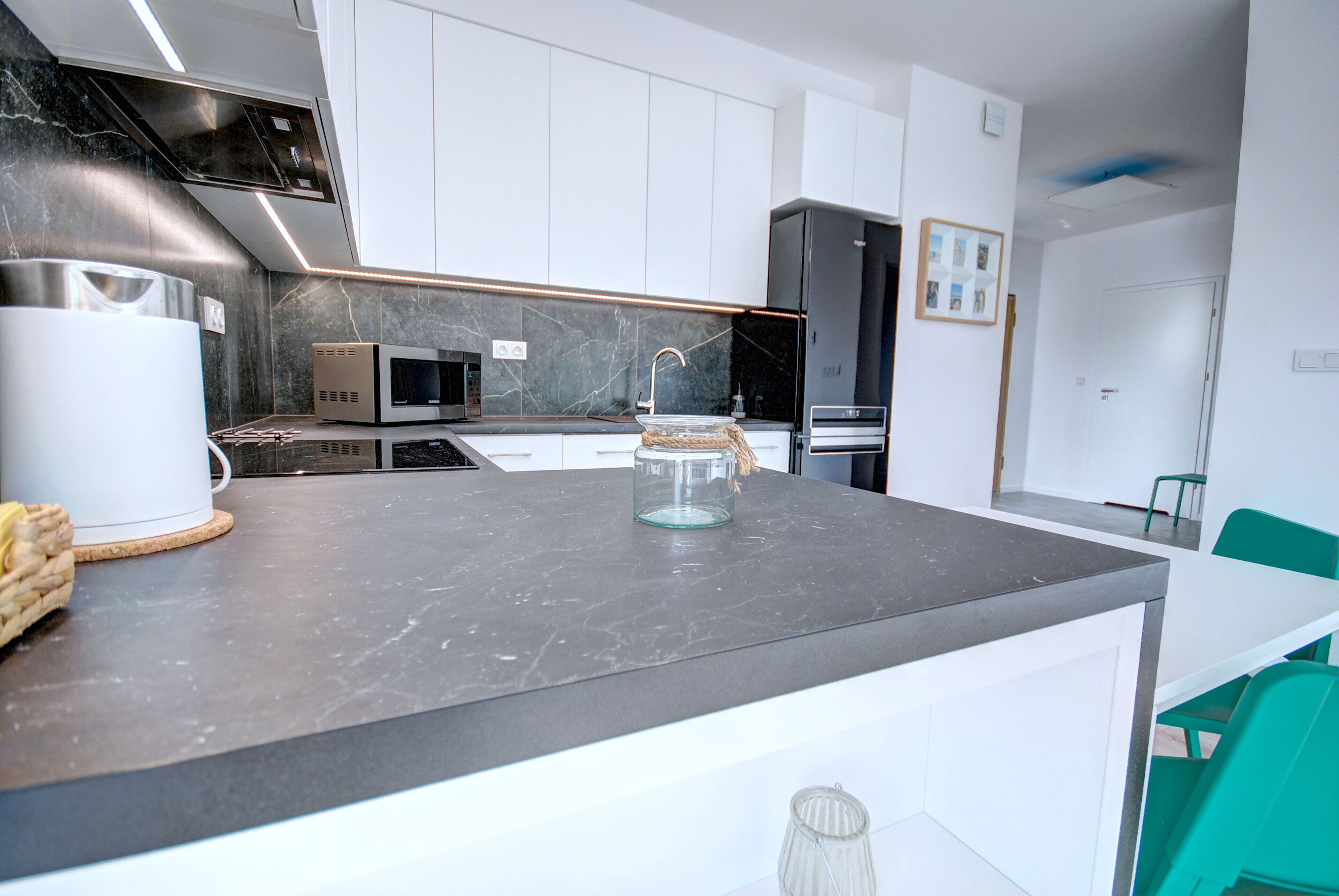 A modern kitchen with white cabinets, a marble countertop, and a built-in microwave.