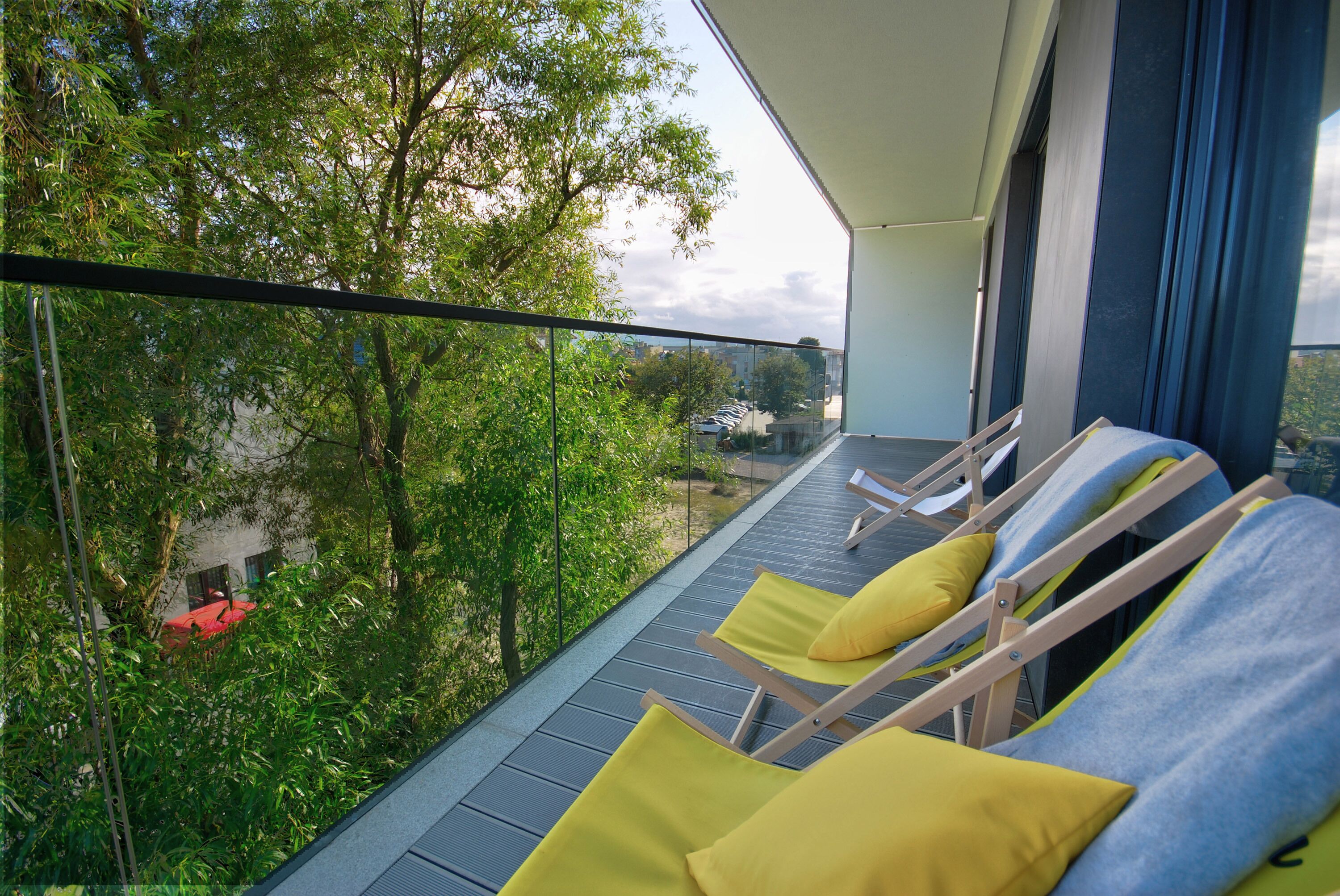 Un balcon avec deux fauteuils de jardin, l’un doté d’un coussin jaune et l’autre d’un coussin bleu.