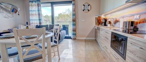 Una cocina moderna con horno empotrado, una zona de comedor con mesa y sillas, y un amplio ventanal con cortinas.