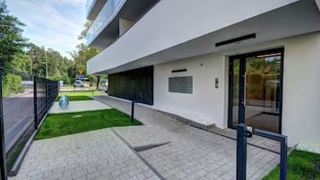 Un edificio moderno con un sendero pavimentado, una cerca metálica y una zona ajardinada.