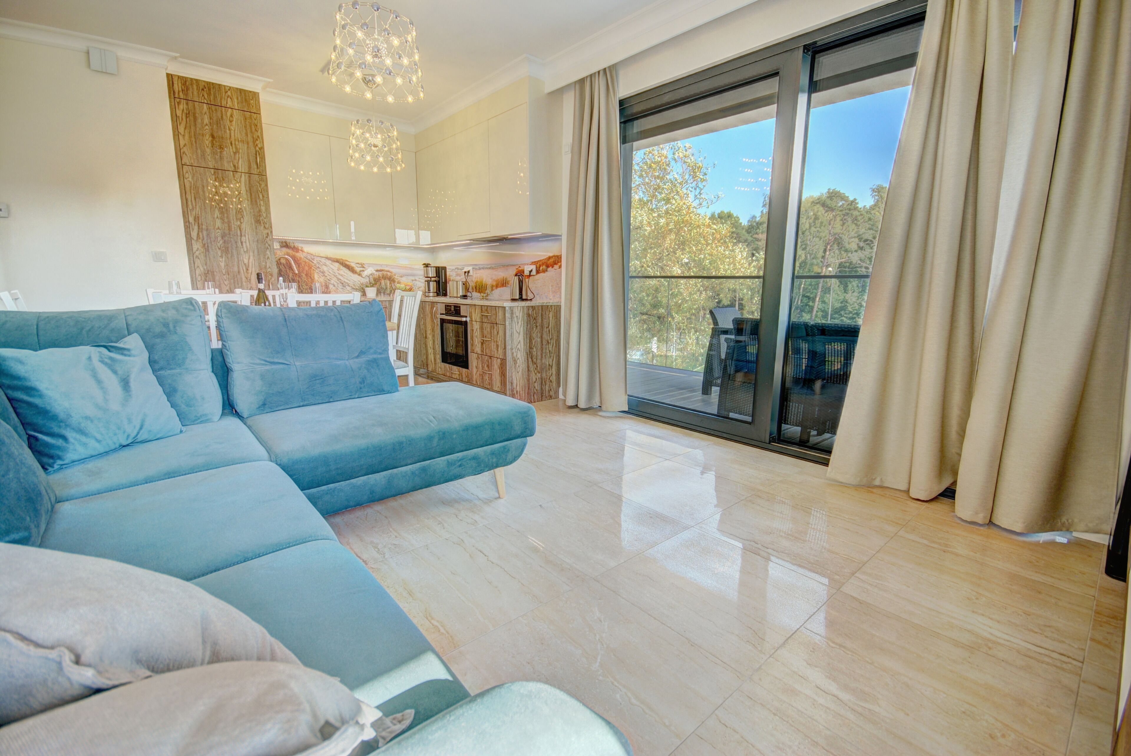 Una sala de estar moderna con un sofá azul, un comedor y una cocina al fondo, además de un balcón con cortinas.