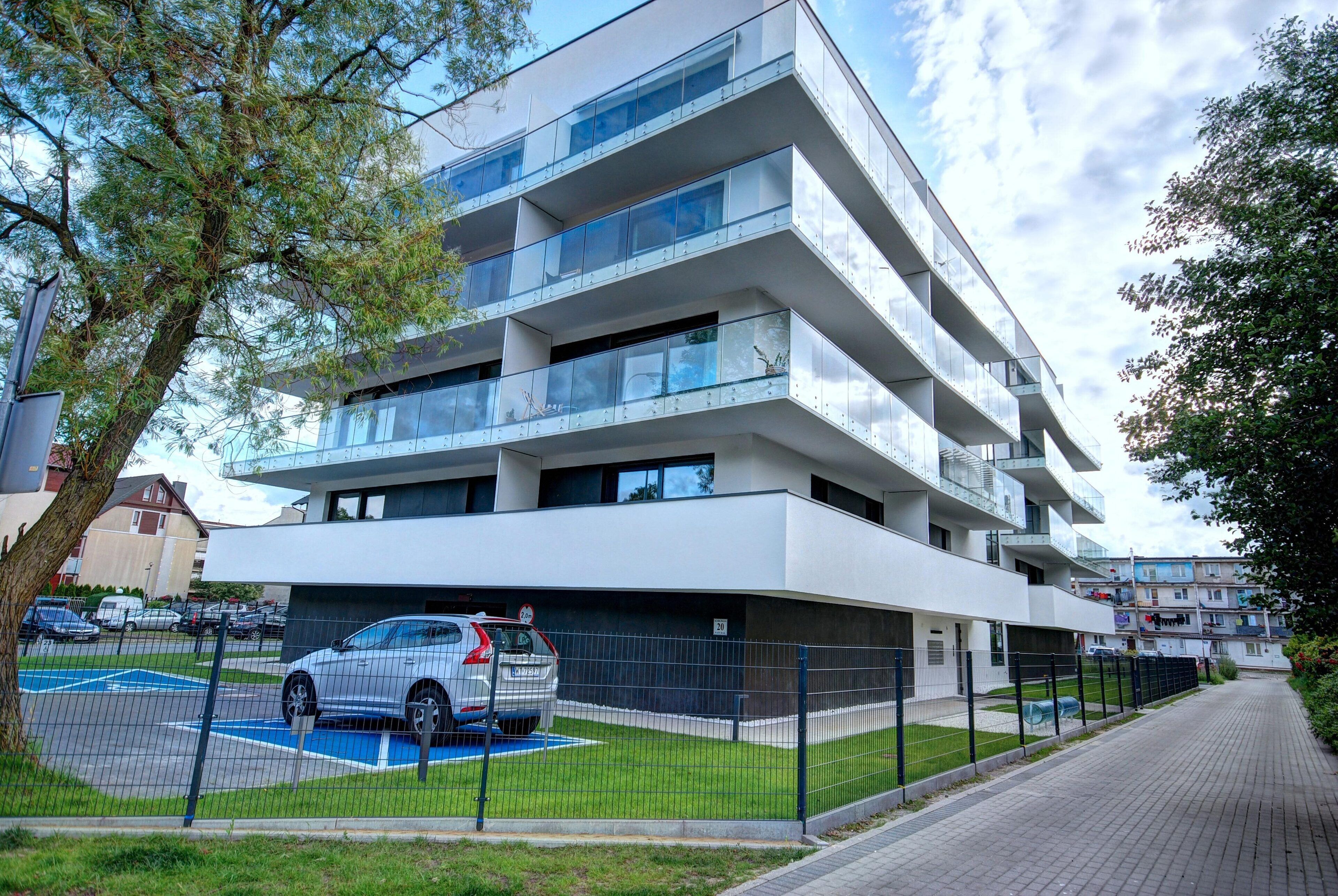 Um edifício moderno de vários andares com área de estacionamento e uma passarela cercada.