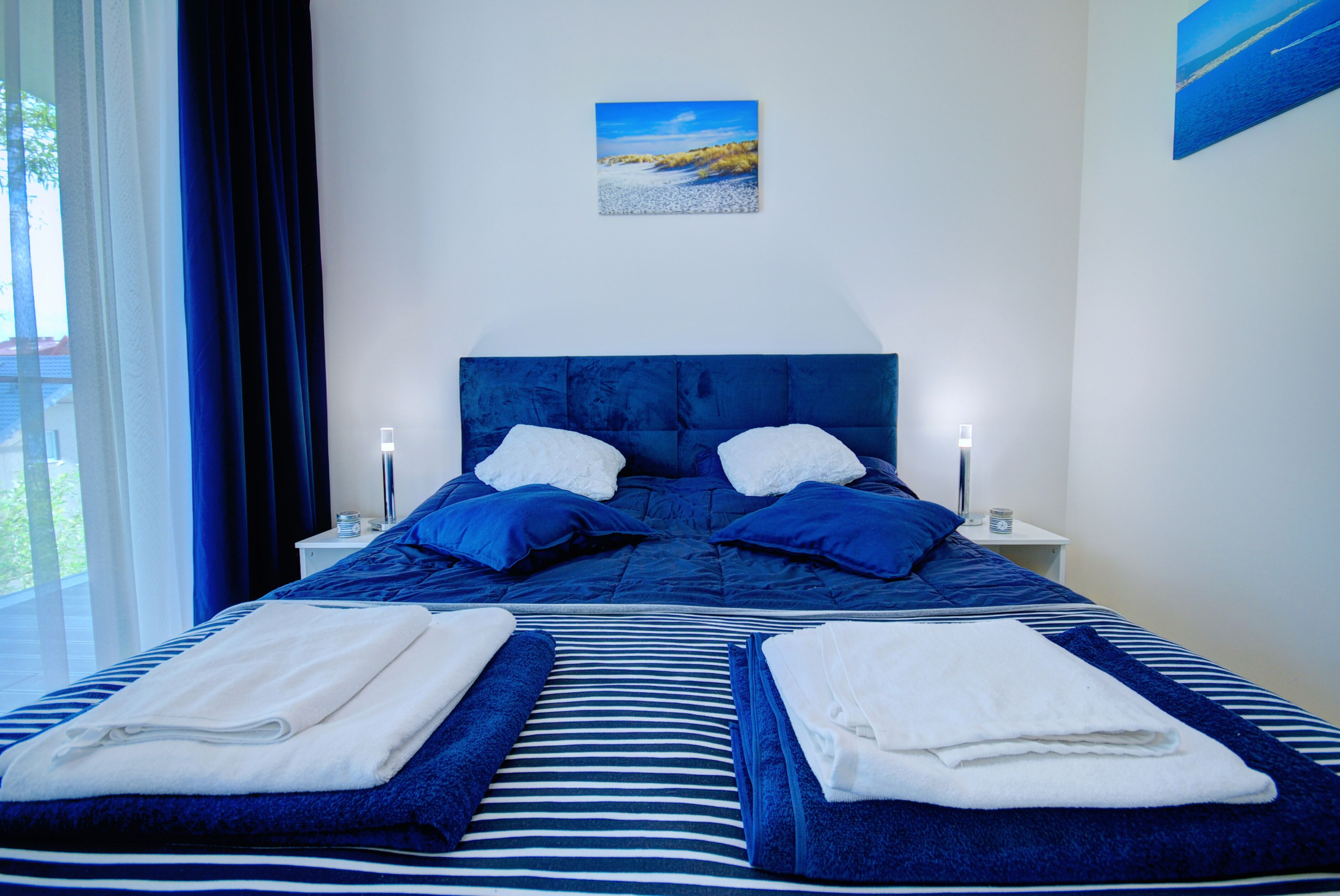 A hotel room with a large bed, two bedside tables, and a window with curtains.