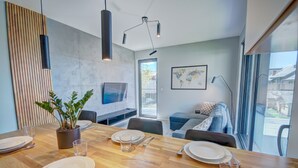 A modern dining area with a wooden table set for four, a potted plant, and a large window offering a view of the outside. - HelApart - NATURALnie że Hel (Hel)
