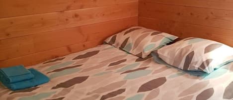 A single bed with a leaf-patterned bedspread and pillows, a wooden headboard, and a small folded towel on the bed.