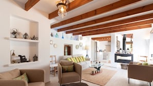 A spacious living room with wooden beams, a sofa, armchairs, and a coffee table.
