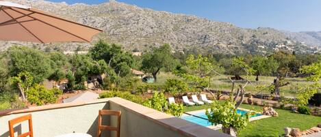 A terrace with a table and chairs, a pool, and a view of a mountainous landscape.