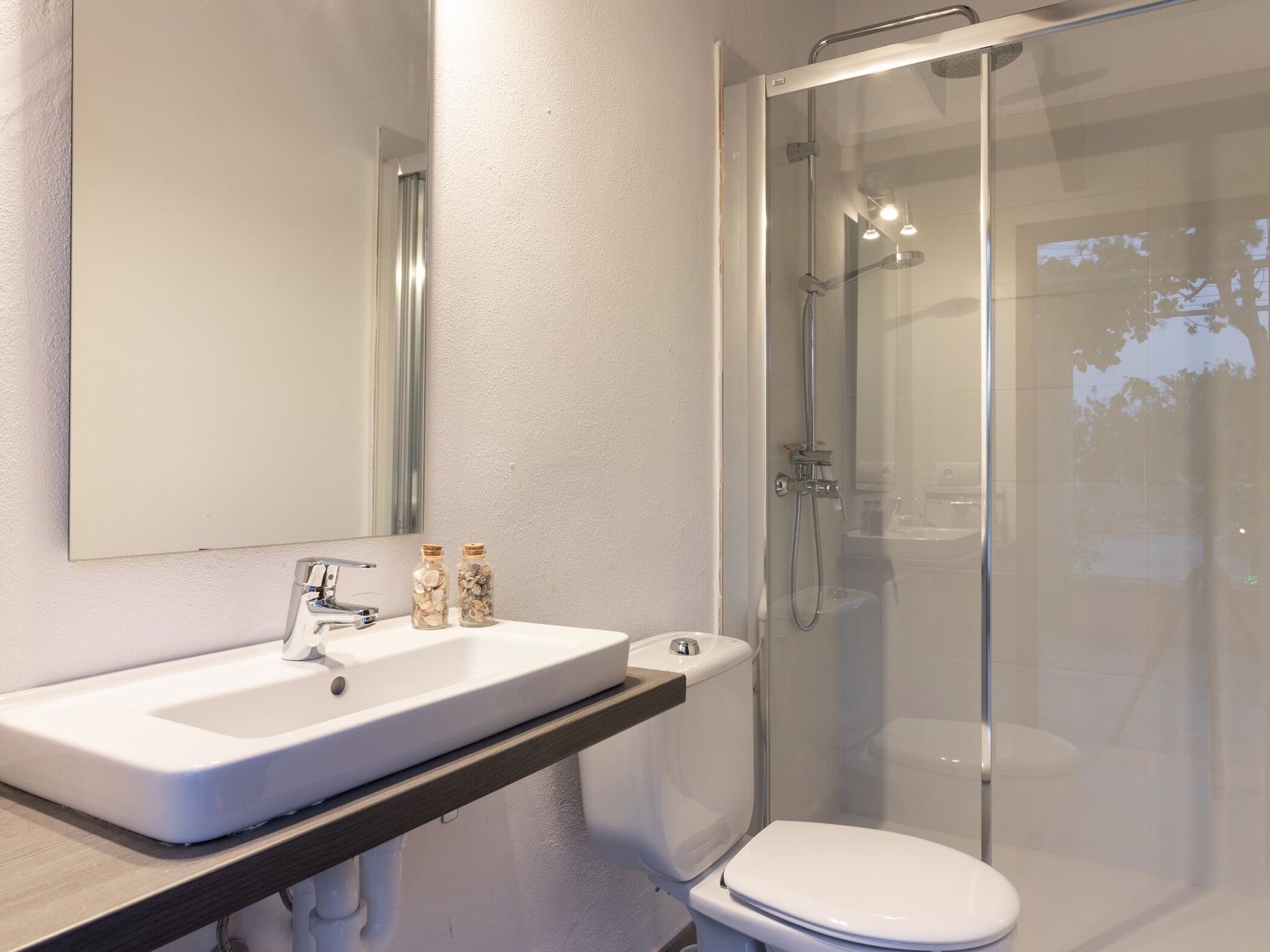 Een moderne badkamer met een witte wastafel, een spiegel en een douche met glazen wanden.