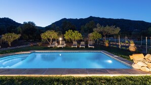 A rectangular swimming pool with a stone border, surrounded by a well-maintained lawn and trees.