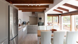 A modern kitchen with a stainless steel refrigerator, white cabinets, and a wooden dining table with white chairs.