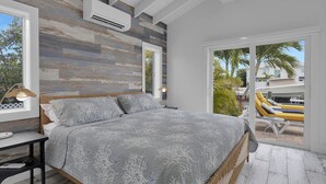 A bedroom with a bed, bedside tables, an air conditioning unit, and a view of a pool area. - The Good Life 5bed/4bath wth private pool 30 ft of dock and 2 kayaks included (Marathon)