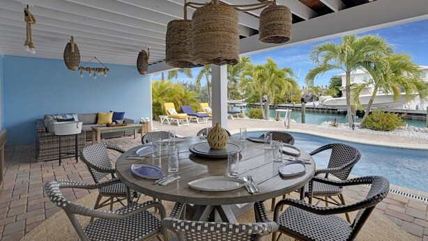 A round table with chairs, a hanging light fixture, and a view of a pool and palm trees. - The Good Life 5bed/4bath wth private pool 30 ft of dock and 2 kayaks included (Marathon)